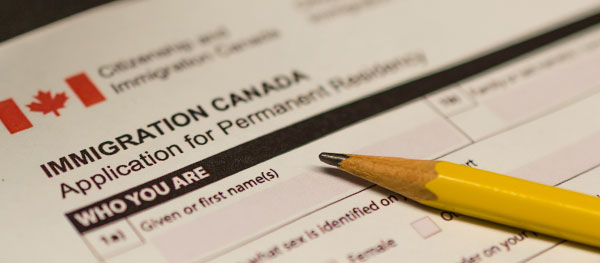 Close-up of the immigration application paperwork for Canada with a pencil laying on top. Image is in full colour