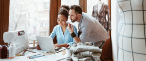 Two people looking at a laptop on a desk. Image is in full colour.